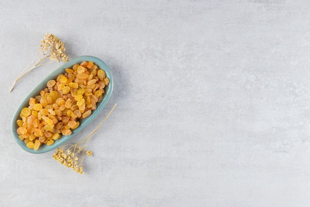 Tas de raisins secs jaunes à bord avec des fleurs séchées placées sur une table en pierre.