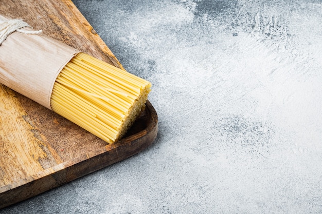 Tas de spaghettis, pâtes italiennes crues, sur plateau en bois, sur fond gris