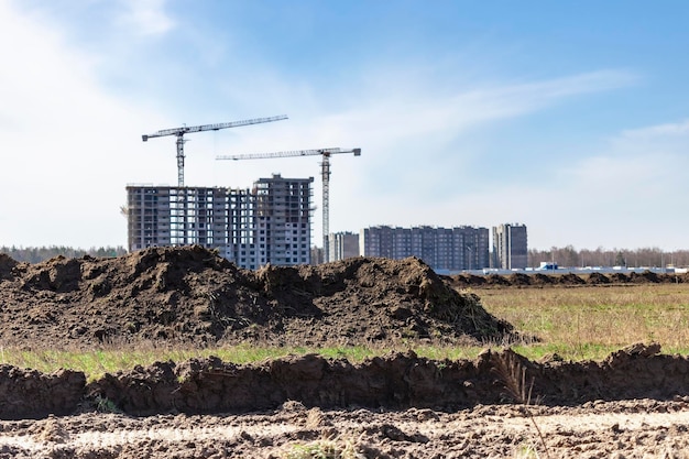 Un tas de terre creusé dans une tranchée contre un ciel bleu nuageux et des chantiers de construction avec une grue à tour