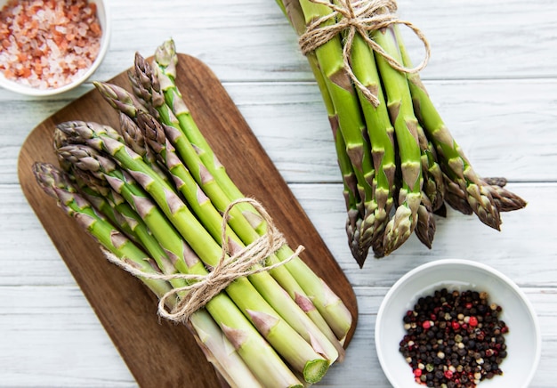 Tas de tiges d'asperges crues avec différentes épices et ingrédients sur fond de bois