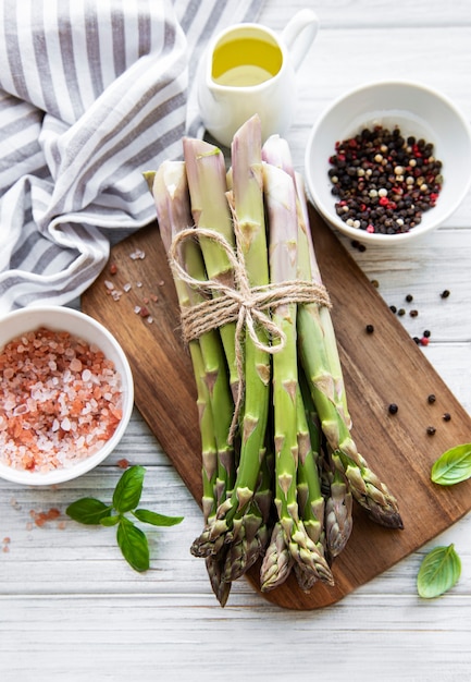 Tas de tiges d'asperges crues avec différentes épices et ingrédients sur une surface en bois