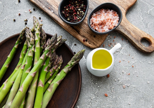 Tas de tiges d'asperges crues avec différentes épices et ingrédients sur table en béton gris. Vue de dessus, pose à plat.