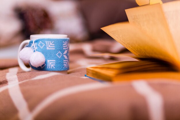 Une Tasse Au Décor Du Nouvel An Se Dresse Sur Un Plaid Marron à Côté D'un Livre Ouvert Sur Fond D'arbre Du Nouvel An. Notion De Nouvel An. Photo