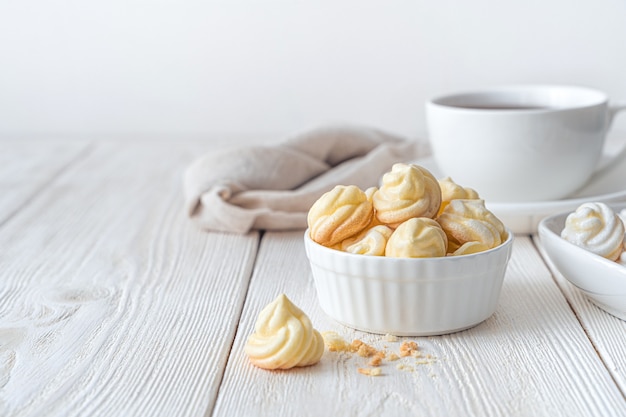 Une tasse aux meringues jaunes sur fond blanc. Vue latérale, horizontale.