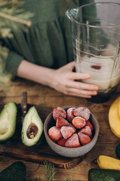 Une tasse de baies congelées préparées pour un smoothie se tient sur la table à côté d'un avocat