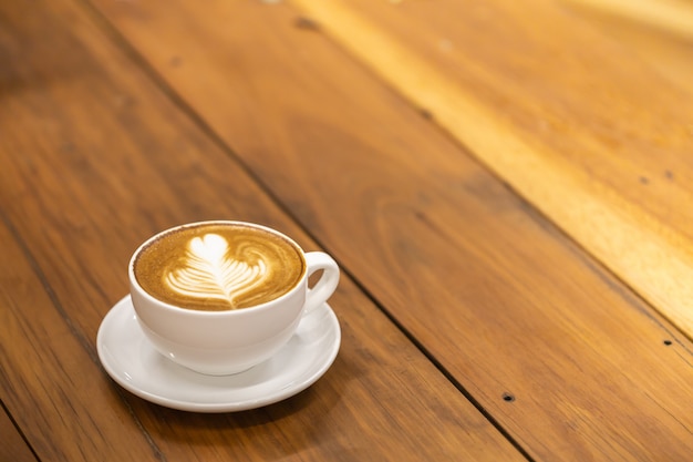 tasse blanche de café au lait chaud avec forme de coeur et art de la fleur sur la table en bois.