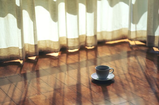 Photo une tasse blanche de café chaud sur un plancher en bois par le rideau de la maison