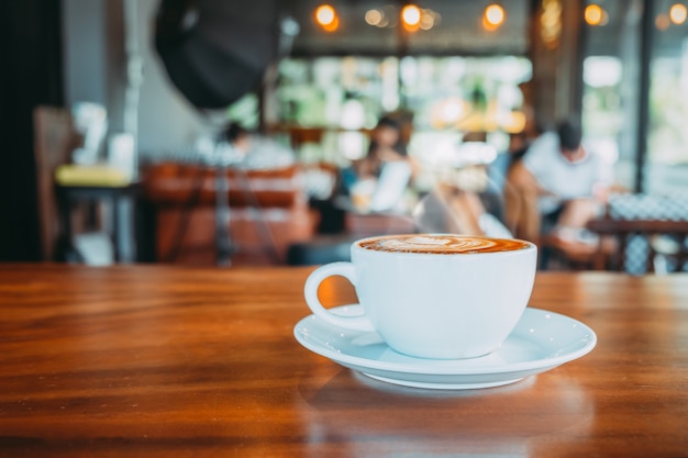 Tasse blanche de café chaud sur la table dans le café avec des gens