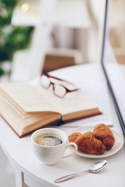 Tasse blanche de café et un livre ouvert sur la table dans une pièce lumineuse