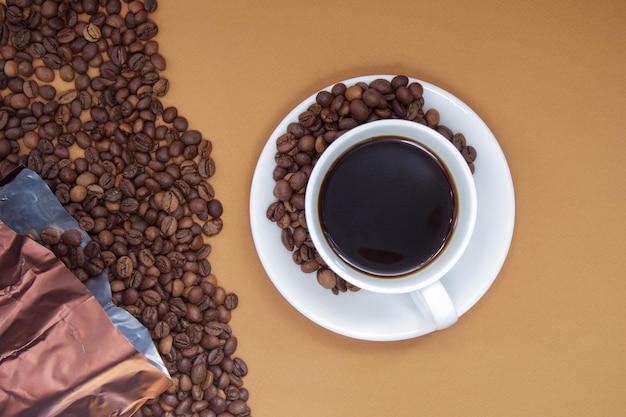 Tasse blanche de café noir Americano sans lait avec un tas de grains de café torréfiés éparpillés dans des emballages en papier. Fond de café, vue de dessus avec espace de copie pour le logo ou le texte.