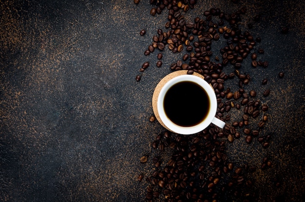 Tasse blanche de café noir et grains de café sur fond de béton foncé. Le concept de boissons chaudes, Petit déjeuner revigorant.