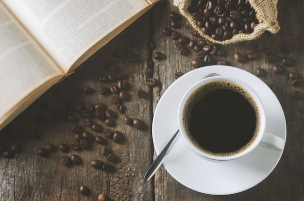 Tasse blanche de café noir sur une table en bois avec grains de café et livre