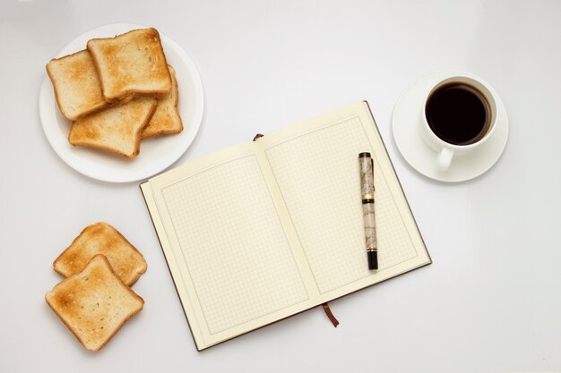 Tasse blanche avec café noir, toasts sur une plaque blanche, bloc-notes sur un blanc. Concept d'un petit-déjeuner de printemps sain