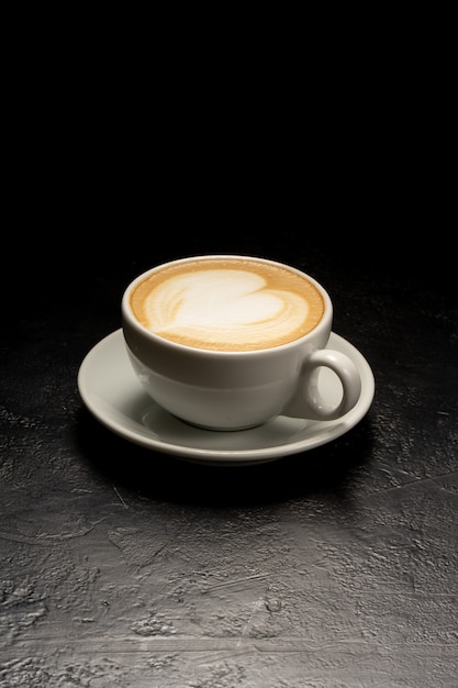 Tasse blanche de cappuccino avec un dessin de coeur. Une tasse de café sur une table noire.