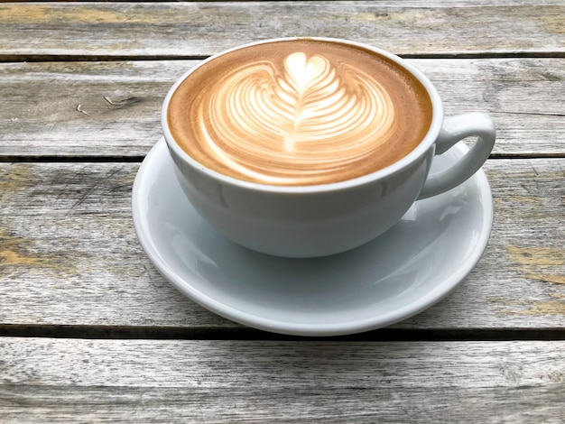 Une tasse blanche de cappuccino avec latte art sur fond de table en bois