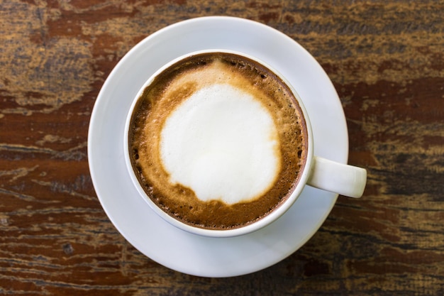 Une tasse blanche de cappuccino sur une soucoupe et sur une table en bois marron. Vue de dessus.