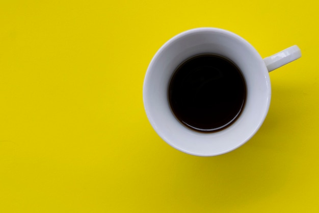 Tasse blanche avec du café sur le panneau jaune. vue de dessus