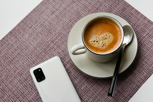 Tasse blanche avec du café et un téléphone sur une vue de dessus de fond violet