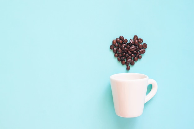 Tasse Blanche Avec Des Grains De Café Disposés En Forme De Coeur Sur Fond De Couleur Pastel