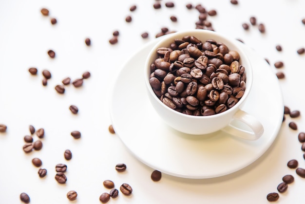 Tasse blanche et grains de café sur fond blanc. Mise au point sélective.