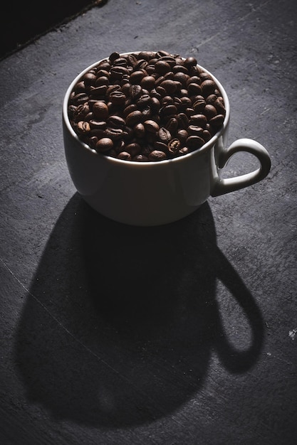 Tasse blanche de grains de café torréfiés fraîchement moulus sur fond gris