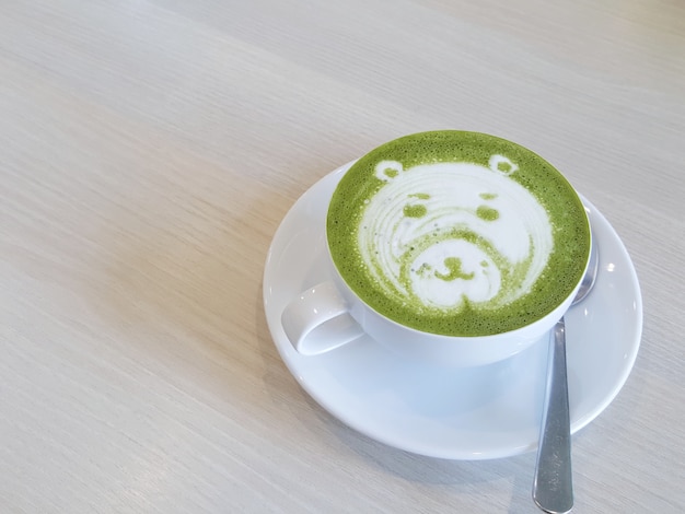 Une tasse blanche de matcha latte avec une mousse d’art décorée de motifs d’ours est placée sur le