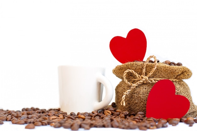 Une tasse blanche et des papiers coeur rouge sur fond blanc de sac de toile de jute de café.