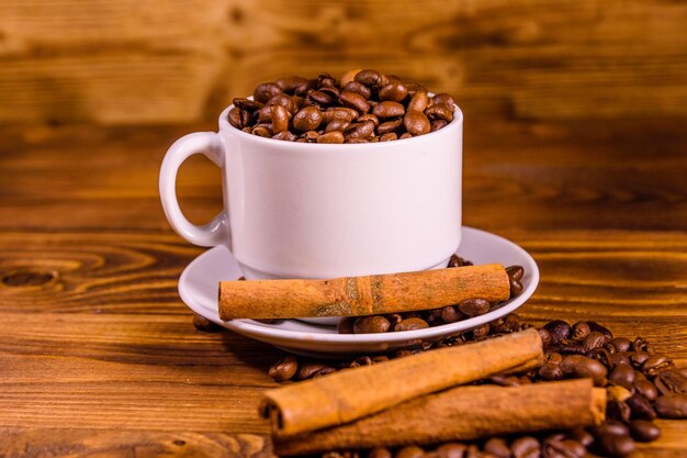 Tasse blanche remplie de grains de café et de bâtons de cannelle sur une table en bois rustique