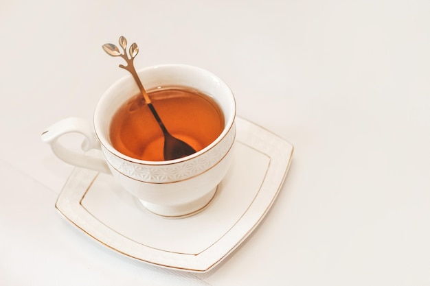 Tasse blanche avec soucoupe et cuillère dorée et feuilles de thé