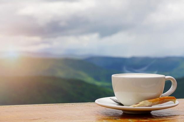 Une tasse blanche de tasses à café expresso chaudes placées sur un plancher en bois avec du brouillard matinal et des montagnes avec la lumière du soleil backgroundcoffee morning