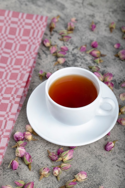 Tasse blanche de thé chaud avec des roses en herbe sur fond de pierre.