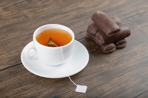 Une tasse blanche de thé noir avec des bâtonnets de chocolat placés sur une table en bois.