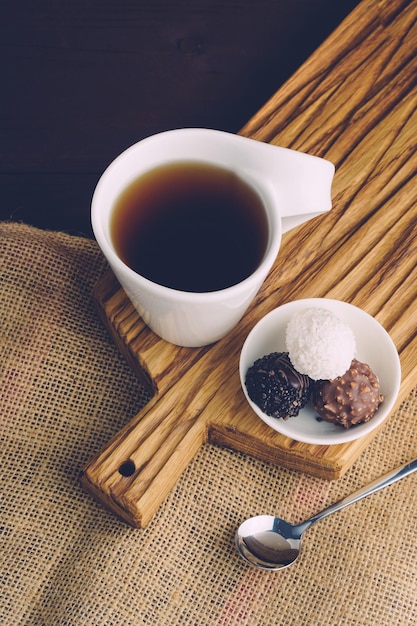 Tasse blanche de thé noir avec cuillère et bonbons sur un bureau en bois Dessert sucré avec concept de thé