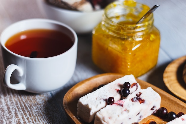 Tasse blanche de thé noir avec guimauve aux baies et pot de confiture d'orange se bouchent. Jeu de freins à thé.