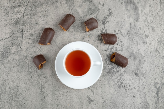 Une tasse blanche de thé savoureux chaud avec des bâtonnets de chocolat sur une table en marbre.