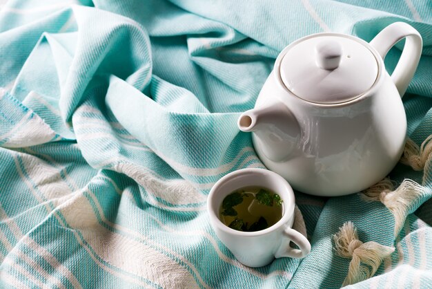 Tasse blanche et théière avec plaid bleu sur un lit