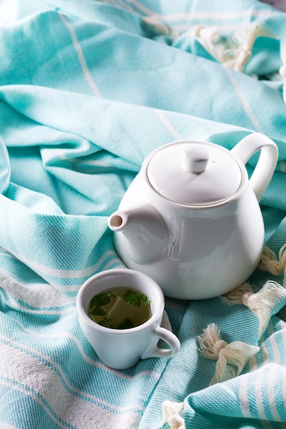 Tasse blanche et théière avec plaid bleu sur un lit