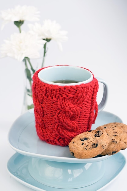 Tasse bleue avec couvercle en tricot rouge et biscuits au chocolat