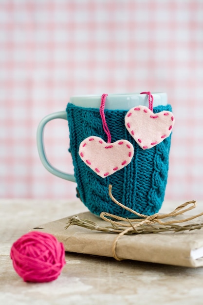 Tasse bleue dans un pull bleu avec des coeurs en feutre