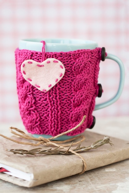 Tasse bleue dans un pull rose avec des coeurs en feutre