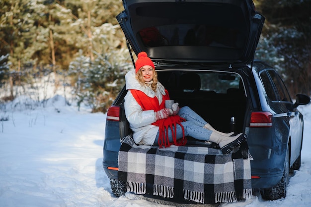 Avec une tasse de boisson Belle jeune femme est à l'extérieur près de son automobile à l'heure d'hiver