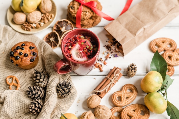 Tasse avec boisson chaude, biscuits, cupcake, noix, clémentines, pommes de pin et bâtons de cannelle sur tableau blanc