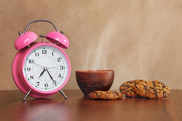 Tasse avec boisson chaude café ou thé et biscuits sur la table près de l'horloge