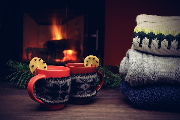 Tasse de boisson chaude devant une cheminée chaude Pile de chandails tricotés confortables