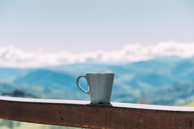 Tasse de boisson chaude placée sur une clôture en bois contre un magnifique paysage de montagne aux beaux jours