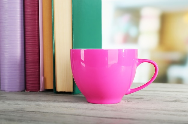 Tasse de boisson de couleur avec des livres sur la table en bois