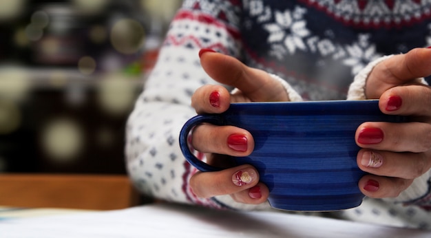 Une tasse de boisson dans les mains d'une fille dans un pull. Ambiance d'hiver confortable. Manucure du nouvel an.