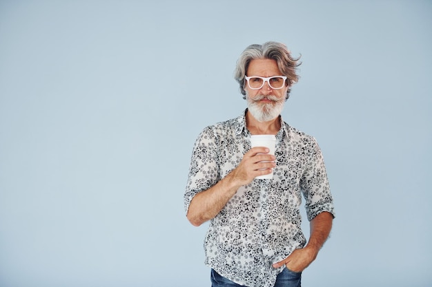 Tasse de boisson dans les mains Senior homme moderne et élégant aux cheveux gris et à la barbe à l'intérieur