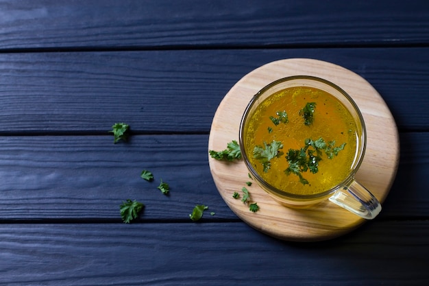 Une tasse de bouillon de poulet chaud, aux herbes, sur une planche de bois. Vue de dessus.