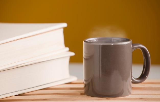 Tasse brune de café ou de thé avec de la vapeur chaude sur la table avec un livre et un fond marron